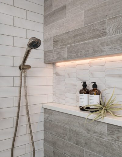 A white tiled shower with a shower head and soap dispenser.