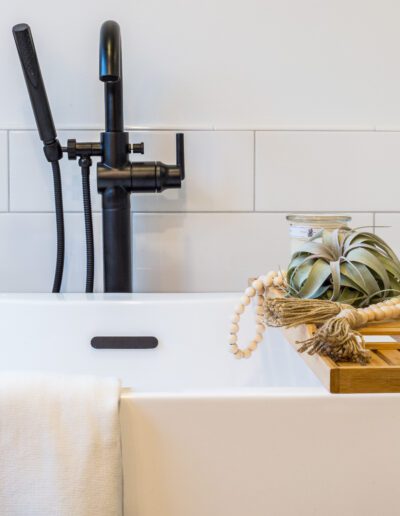 A white bathroom with a wooden tray and a black faucet.