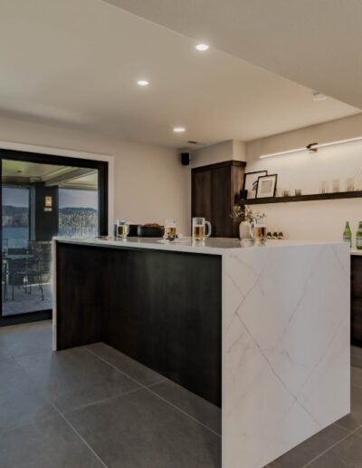 Modern kitchen with marble island, dark wood cabinets, and a view of a lake through sliding glass doors leading to a balcony.