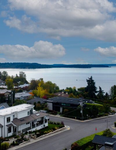 Aerial view of a residential area with houses lining streets near the shore of a vast blue lake, under a partly cloudy sky.