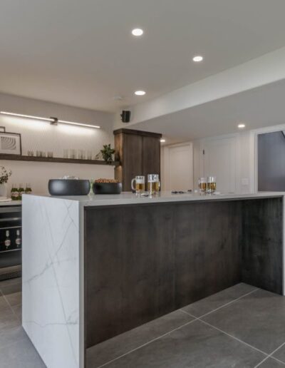 Modern kitchen with dark wood cabinets, a central island with a marble countertop, built-in appliances, and stairway leading upstairs.