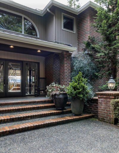 Elegant brick house with a cobblestone driveway, arched windows, and lush greenery surrounding the entrance.