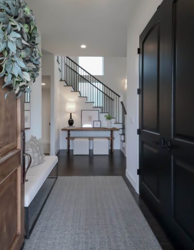 Elegant entryway featuring a black door, a console table with decoration, a gray rug, and a staircase with black railings.