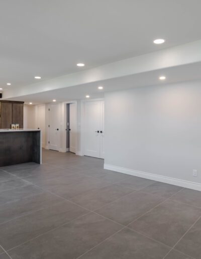 Modern kitchen with a breakfast bar, dark wood cabinetry, built-in appliances, and gray tiled flooring in a spacious room with white walls and recessed lighting.