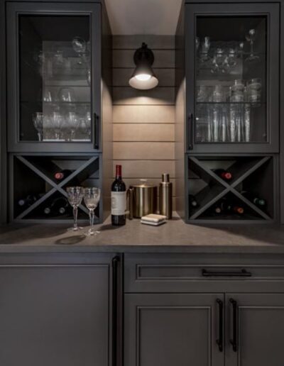 A home bar features glass cabinets with wine storage, two glasses, a wine bottle, and metallic containers on a countertop under ambient lighting.