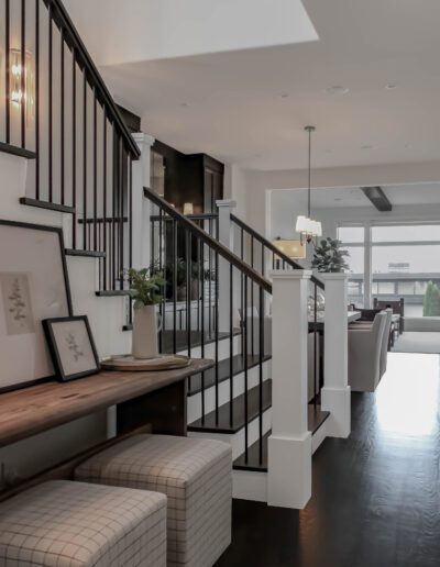 An elegant interior showing a wooden staircase with black metal railings beside a modern bench, leading to a bright open-plan living space.