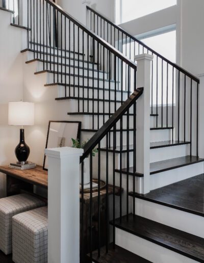 A modern staircase with white walls, dark wooden steps, and black metal railings. the scene includes a small seating area under the stairs.