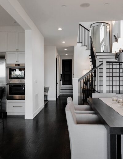 Modern home interior featuring a stairway with black railings, a kitchen on the left, and dark hardwood floors, viewed from the living area.