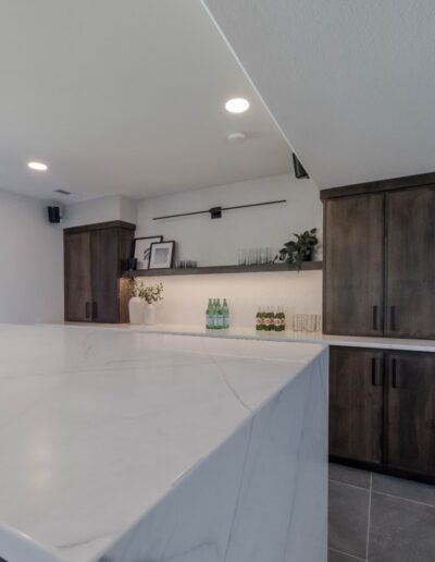 Modern kitchen with white marble countertop, dark wooden cabinets, and decorative plants on the counter.