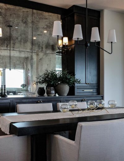 Elegant dining room with a black wooden table, surrounded by light grey chairs, dark cabinetry, and stylish pendant lights.