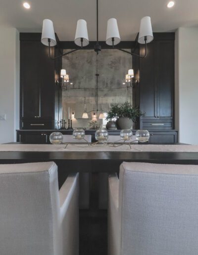 A modern dining room featuring a dark wooden table surrounded by light grey chairs, a mirror wall decor, and a linear chandelier with white shades.