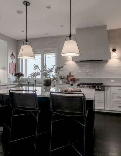 Modern kitchen interior with white cabinetry, stainless steel appliances, and a central island featuring bar stools under pendant lights.