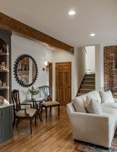 Cozy living room with a brick fireplace, built-in shelves with collectibles, wooden beams, and comfortable seating area.