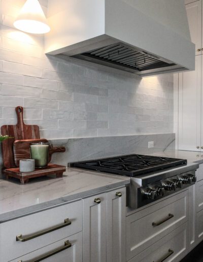 Modern kitchen interior featuring a gas stove and a stainless steel range hood, with white cabinetry and gray backsplash tiles.