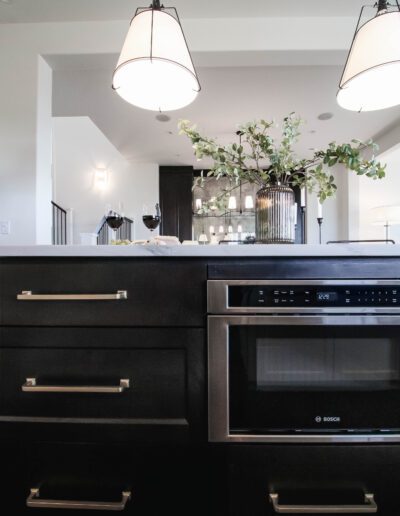 Modern kitchen interior with black built-in oven and cabinets, featuring a white countertop and hanging pendant lights.