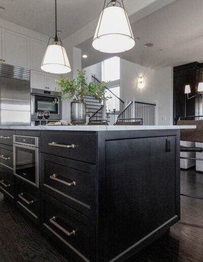 Modern kitchen with black cabinetry, white countertops, stainless steel appliances, pendant lighting, and a dark hardwood floor.