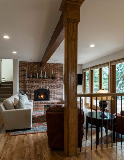 Spacious living room with a brick fireplace, wooden floors, exposed beams, and modern furniture. glass doors provide natural light.