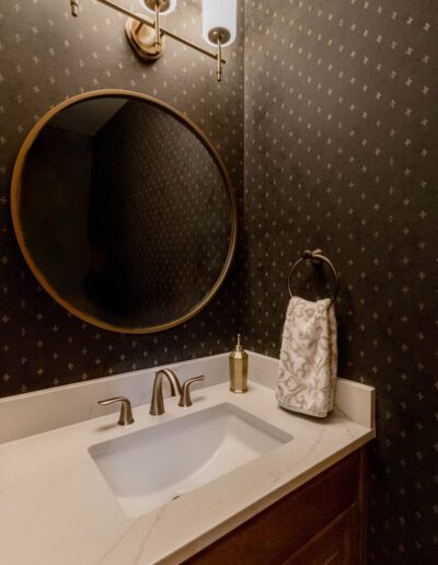 A modern bathroom with a round mirror and white sink, under a dark star-patterned wallpaper, illuminated by two wall lamps.