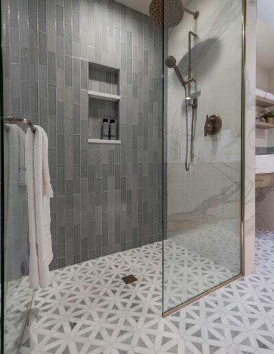 Modern bathroom with a glass shower enclosure, gray tile walls, and a patterned white floor. a built-in shower niche holds toiletries.