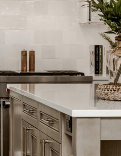 A modern kitchen with a stainless steel oven, white countertops, beige cabinets, and a decorative vase with green foliage on the island.