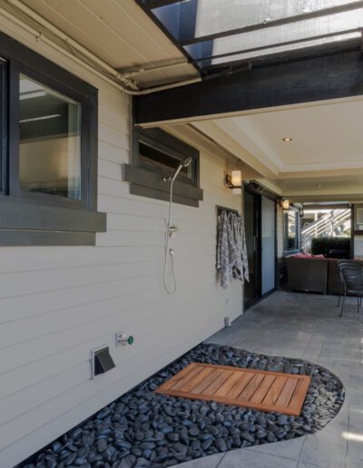 Modern patio area with stone flooring, outdoor furniture, and an open-air living space with a television set mounted on a white siding wall.