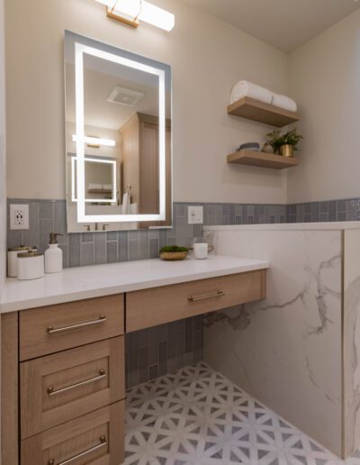 Modern bathroom interior featuring a vanity with wooden cabinets, marble countertop, and reflective mirror, complemented by patterned tile flooring and floating shelves.