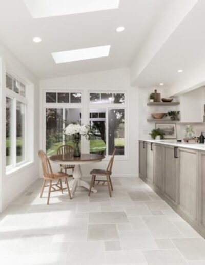 Bright kitchen with skylights, white cabinetry, and a kitchen island. A round dining table with chairs is positioned near large windows and a glass door with a view of the outdoors.