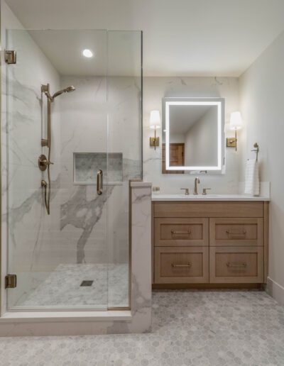 Modern bathroom featuring a glass shower enclosure, marble walls, wooden vanity with double sinks, and hexagonal tile flooring.