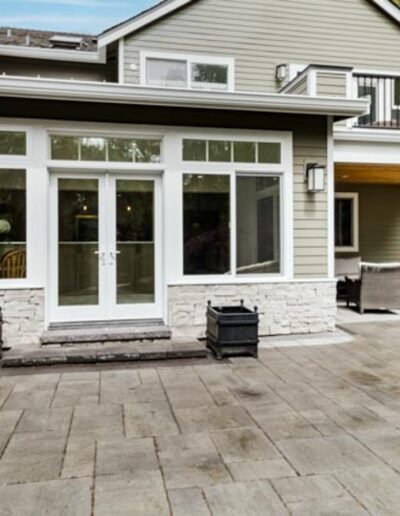 A modern two-story house with large windows, stone trim, and an outdoor patio area with seating.