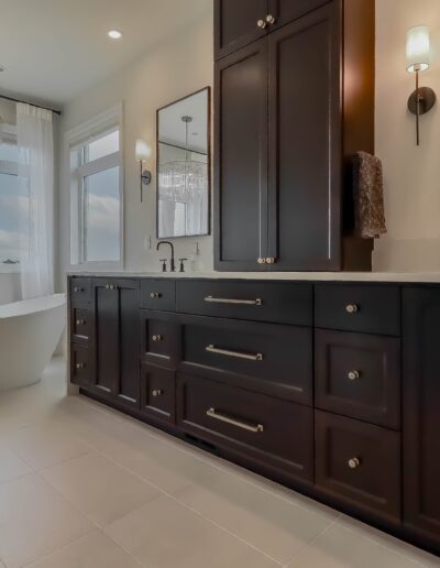 A luxurious bathroom with dark wood cabinets, dual sinks, large mirrors, and a freestanding tub by a window with ocean view.