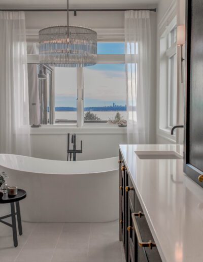 Luxurious bathroom with a freestanding tub, crystal chandelier, and a panoramic view of a lake through large windows.