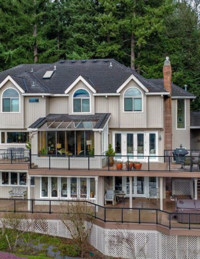 Aerial view of a large two-story house with multiple balconies and decks, surrounded by dense trees.