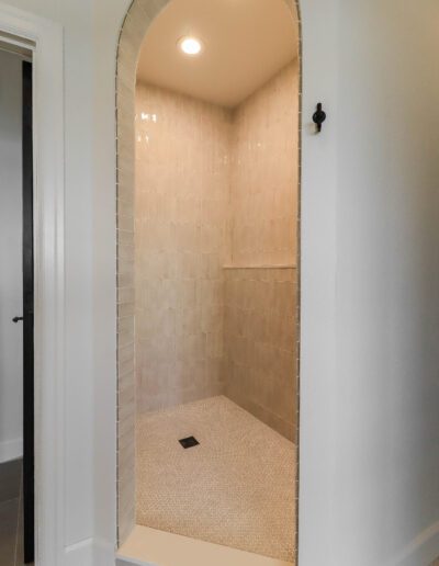 A modern bathroom with a doorless walk-in shower featuring beige tiles and a small, dark floor drain.