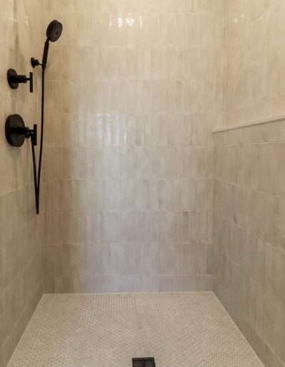 Empty modern shower with white tiled walls and hexagonal floor tiles, featuring a black shower head and handle.