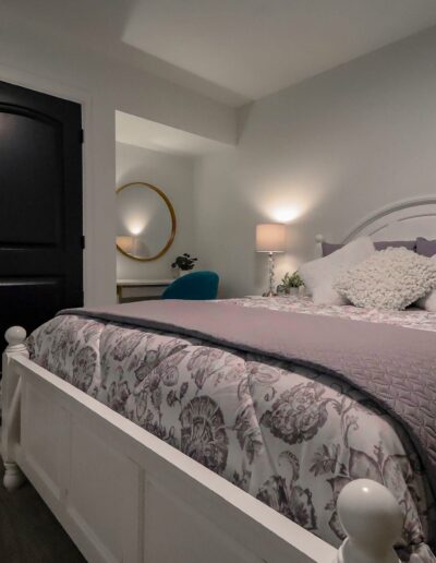 A modern bedroom with a white and purple floral-patterned bed, black doors, and a circular mirror on a gray wall.