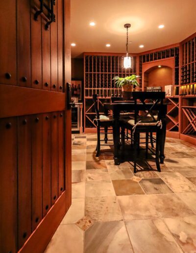 A cozy home library with wooden shelves, a central reading table, warm lighting, and a stone floor, viewed from an open wooden door.