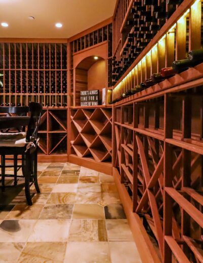 Interior of a wine cellar with wooden racks full of bottles, a tiled floor, and a small bar area with stools.