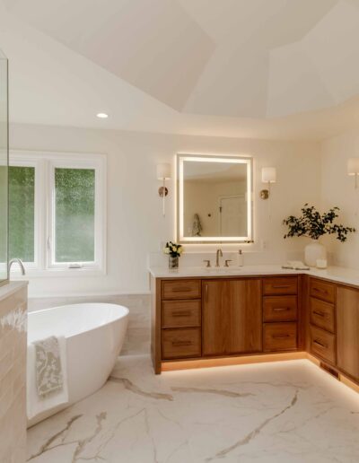 Modern bathroom with a freestanding tub, glass shower, double vanity with illuminated mirrors, wooden cabinets, and recessed lighting.