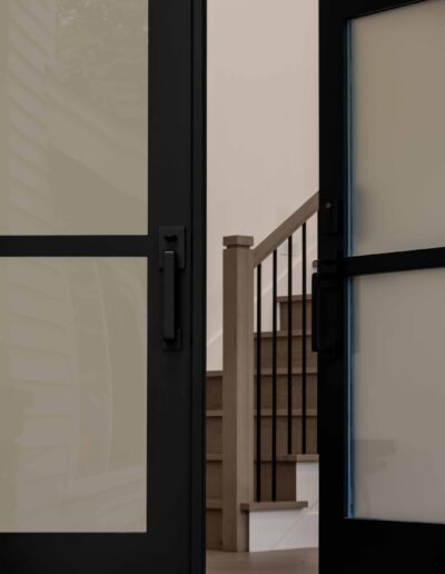 Partially open black-framed glass door revealing indoor staircase with wooden steps and black handrail.