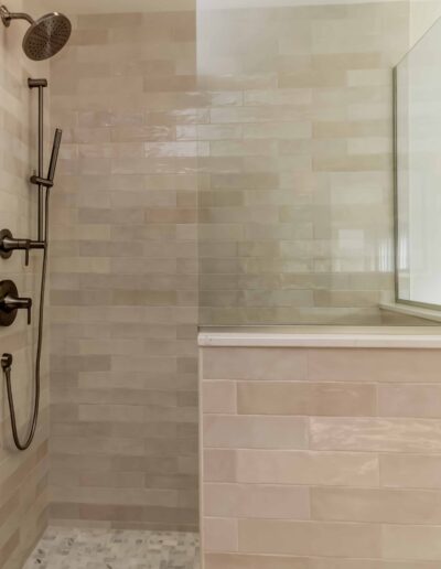 Modern shower with beige tiles, glass partition, and wall-mounted showerhead with controls.