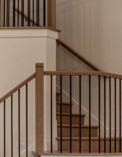 A wooden staircase with black metal railings, featuring a landing midway and light-colored walls.