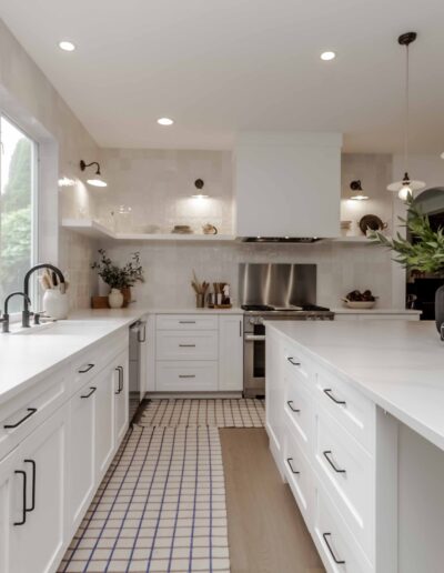 A modern, bright kitchen with white cabinets, two large islands, pendant lights, and decorative plants.