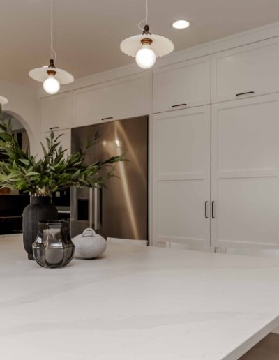 Modern kitchen with white cabinets, a large island, pendant lights, and an open pantry showcasing various food items.