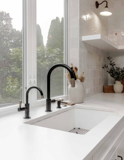 A kitchen with white cabinets and countertops, a black faucet over a sink, and a large window overlooking greenery.