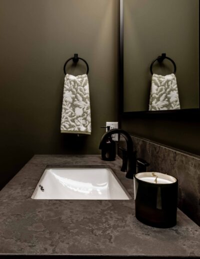 A modern bathroom counter with a rectangular sink, black faucet, candle, and towel hanging on a ring.