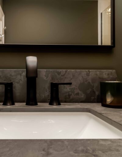 Modern bathroom sink with a dark stone countertop, black faucet fixtures, and a black candle holder, reflected in a mirror.