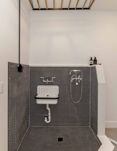 Compact, contemporary bathroom corner with black hexagonal tiles, white wall-mounted sink, and a hanging wooden ceiling rack above.