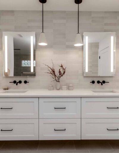 A modern bathroom features a double sink with white cabinets, black fixtures, overhead pendant lights, and wall-mounted mirrors.